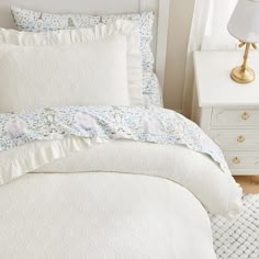 a bed with white sheets and pillows on top of it next to a night stand