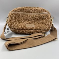 This is a small brown rectangular shoulder bag made of fabric with a solid pattern. It has a zip closure, crossbody strap handle style, and brown cotton lining. The hardware color is gold and the handle/strap color is brown. The brand is Sherpa and the bag features a designer, animals, bohemian, classic, and preppy theme. Casual Brown Shoulder Bag With Zipper Pouch, Brown Shoulder Bag With Zipper Pouch For On-the-go, Brown Zipper Pouch Shoulder Bag For On-the-go, Brown Shoulder Bag With Zipper Pouch For Everyday, Brown Zipper Pouch Shoulder Bag For Everyday, Brown Crossbody Bag With Zipper Pouch, Brown Satchel Shoulder Bag With Zipper Pouch, Brown Pouch Shoulder Bag With Zipper, Brown Crossbody Shoulder Bag With Zipper Pouch