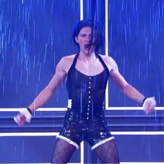 a woman with her arms out in front of a blue background and rain falling down on her