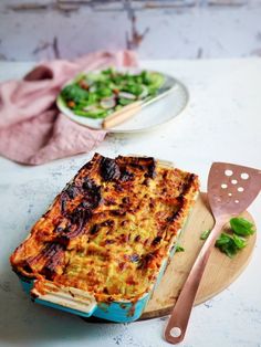 a casserole dish on a cutting board with a spatula next to it