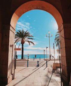 an archway leading to the beach with palm trees on either side and people walking in the distance