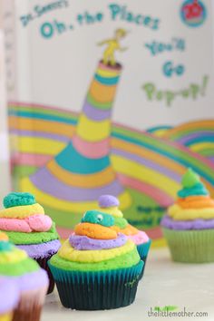 cupcakes decorated with rainbow frosting and dr seuss hat on display in front of children's book