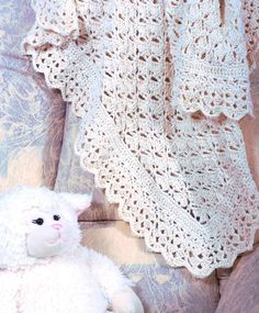 a white teddy bear sitting on top of a couch next to a crocheted blanket