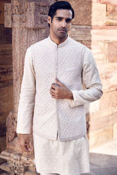 Introducing the regal nayab dandy jacket in ecru raw silk, a pinnacle of sophistication and craftsmanship. Meticulously crafted with off-white cotton thread dori work and exquisite hand highlights, this jacket seamlessly blends traditional and modern elements. Inspired by the spirited wilderness of masai mara, it features decadent floral and paisley embroidery, adding an air of opulence and charm. Designed for those who appreciate fine detail, our jacket is a testament to meticulous craftsmanshi Elegant Chanderi Nehru Jacket For Diwali, Transitional Cream Cotton Silk Sets, White Cotton Nehru Jacket For Festive Occasions, Off White Cotton Silk Long Sleeve Kurta, Eid Cotton Silk Nehru Jacket With Intricate Embroidery, White Cotton Nehru Jacket With Intricate Embroidery, Elegant Chanderi Bandhgala For Transitional Season, White Cotton Silk Bandhgala With Resham Embroidery, Festive White Cotton Nehru Jacket