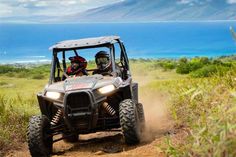 two people riding in the back of a four - wheeled vehicle on a dirt road