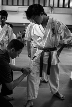 two young men are practicing karate in a gym while another man holds his hand on the belt