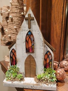 a small white church with stained glass windows on top of a table next to ornaments