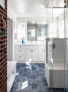 a bathroom with blue tile flooring and white cabinets, along with a brick wall