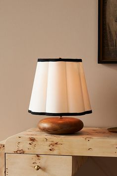 a lamp sitting on top of a wooden table next to a painting and an old dresser