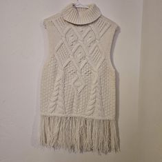 a white sweater with fringes hanging on a wall