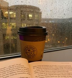 a cup of coffee and an open book on a window sill in the rain