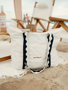 a white tote bag sitting on top of a beach next to a wooden chair