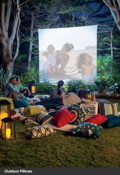 people sitting on the grass watching a movie in front of a large screen with candles