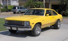 a yellow car parked in front of a building with palm trees and cars behind it