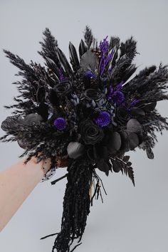 a hand holding a purple and black bouquet with feathers on it's end,