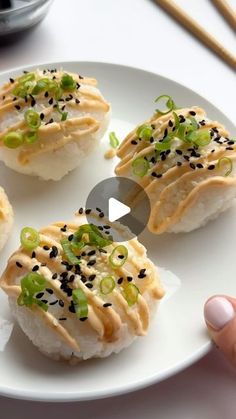 three sushi rolls with sesame seeds and green onions on a white plate next to chopsticks