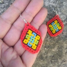 a hand holding two small beaded earrings in it's left hand, one with an orange and yellow square