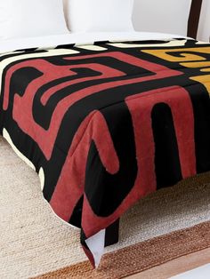 a bed with a black, yellow and red blanket on it's headboard