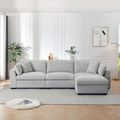 a living room with white walls and wood flooring, a large sectional couch in the middle