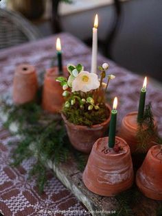 small clay pots with flowers and candles are on a wooden tableclothed table cloth