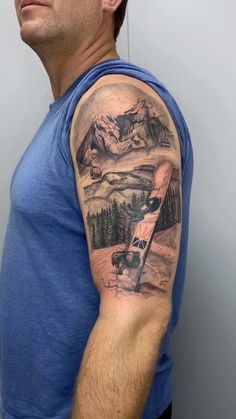 a man wearing a blue shirt has a mountain and airplane tattoo on his left arm