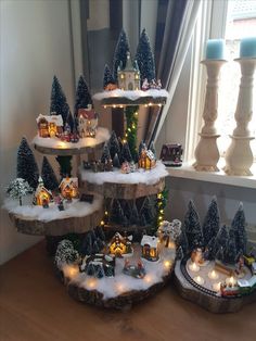 a christmas tree with lights and houses in the snow next to a window sill