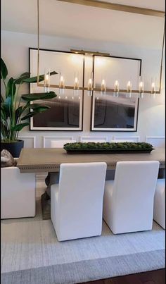 a dining room table with white chairs and two large mirrors above it