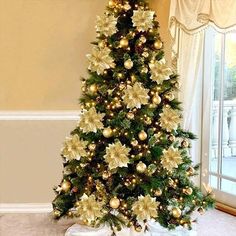 a decorated christmas tree in front of a window with white and gold ornaments on it