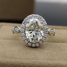 an oval cut diamond surrounded by smaller round diamonds sits on top of a cushioned surface