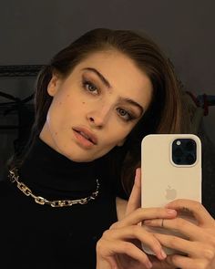 a woman taking a selfie with her iphone in front of her face and wearing a black turtle neck top