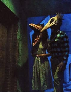 a man and woman standing next to each other in front of a blue wall with an animal mask on it's head