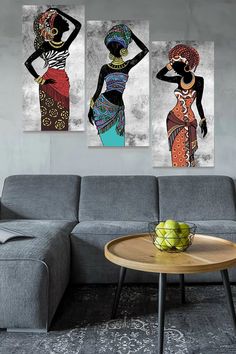 three african women in colorful dresses hanging on a wall above a gray couch and coffee table