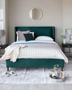 a bedroom with a green bed and white rugs on the floor in front of a round mirror