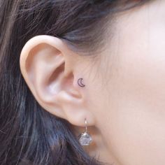 a woman's ear has a small crescent tattoo on it