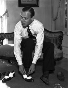 a man sitting on the floor tying his shoes in black and white photo by an antique chair