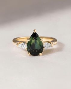 a pear shaped green and white diamond ring with three diamonds on the band, set in yellow gold