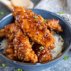 a blue bowl filled with fried chicken and white rice on top of a table next to chopsticks