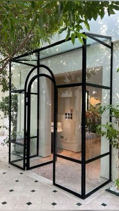 a black and white glass house sitting on top of a tiled floor next to a tree