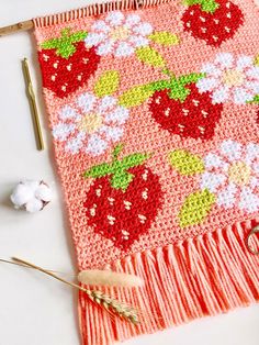 a knitted blanket with strawberries and flowers on it next to cotton floss