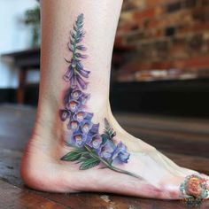 a woman's foot with purple flowers and leaves on the bottom of her leg