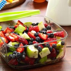 a glass bowl filled with fruit salad on top of a wooden table next to a bottle of milk