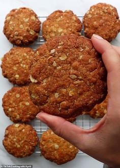 a person holding a cookie in front of some cookies on a cooling rack with nuts