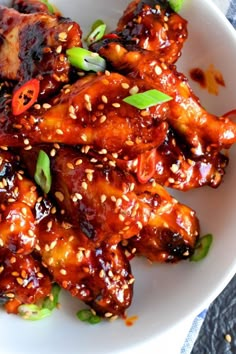 a white plate topped with chicken wings covered in sauce and sesame seeds, garnished with green onions