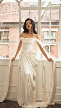 a woman standing in front of a window wearing a white dress and holding her hands on her hips