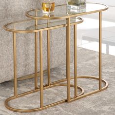 a glass and metal side table with a drink on it in front of a couch