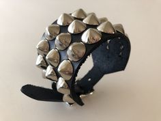 "Black leather studded punk bracelet with 3 rows of cone studs. Cone studs are 1/2\" wide and about 3/8\" tall so bracelet can easily be worn under jacket sleeves. Cone studs are made from high quality nickel plated brass. Buckle and rivets are also nickel plated. Bracelet is 1.75\" wide. Smaller cuff has fewer studs. Made out of hand dyed vegetable tan leather. Ask about custom sizes and colors!" Punk Black Bracelet With Silver Studs, Black Leather Punk Bracelet With Silver Studs, Punk Leather Bracelet With Studs, Punk Style Studded Leather Bracelet, Edgy Leather Bracelets With Studs, Rocker Leather Bracelet With Rivets For Festivals, Black Rocker Bracelet With Studs, Rocker Style Leather Bracelet With Studs For Festivals, Rocker Style Leather Bracelet With Rivets For Concert