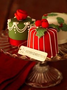 three cakes decorated with holly decorations on a glass cake platter, one is red and the other is green