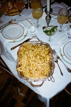 a table topped with plates and silverware covered in french fries on top of a white table cloth