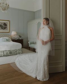 a woman in a white wedding dress standing next to a bed and chandelier