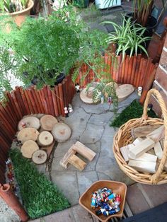 an outdoor area with logs, plants and small figurines on the ground in front of a wooden fence